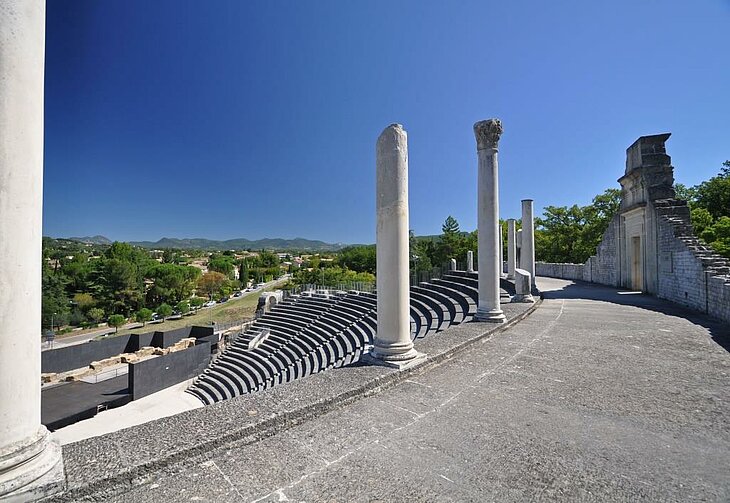 Ancient theatre in Vaison-la-Romaine, with its tiered seating and columns beneath a blue sky, with hills in the background.
