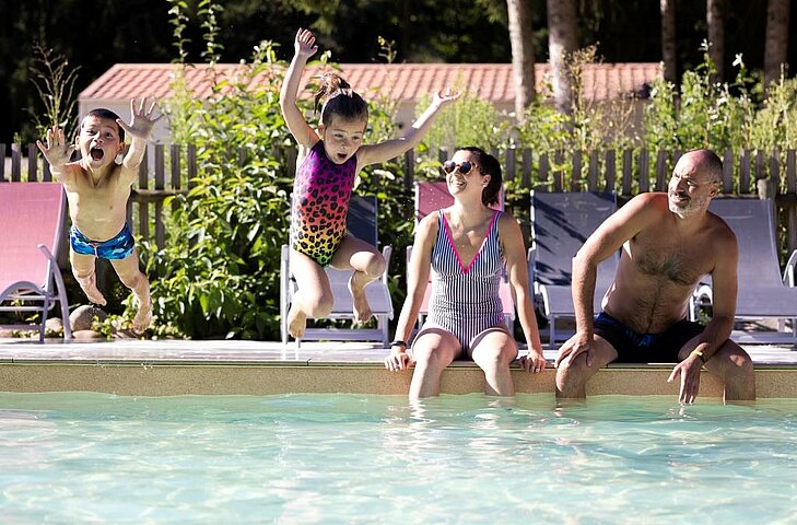 Children jumping into a campsite swimming pool during a budget family holiday with activities included.