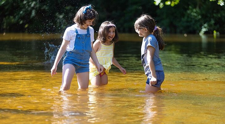 Three children playing and cooling off in a river on a summer’s day.