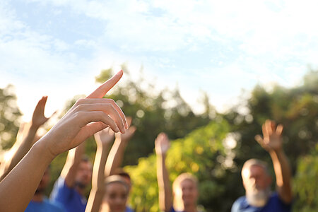 Group of people raising their hands outdoors, symbolizing a collective commitment to purposeful tourism and nature.