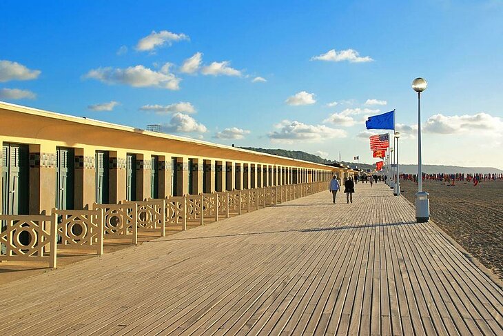 Wooden boardwalk and beach huts in Deauville, Normandy, with flags facing the sea, a friendly outing between friends combining beach and casino.