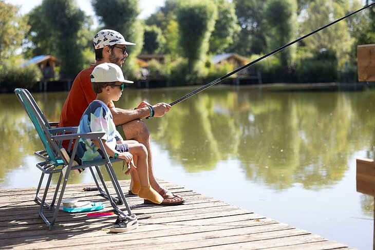 Father and child fishing by a campsite lake, peaceful nature moment supporting well-being and outdoor family time.