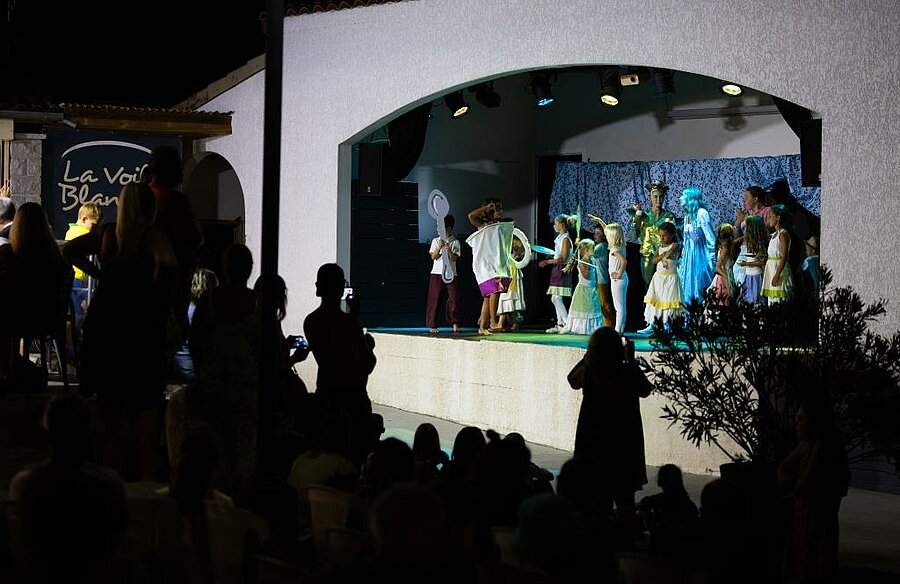 Children performing on stage at a campsite, families enjoying a friendly and optional evening entertainment together.
