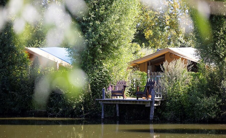 Lodge tent with wooden deck and chairs by a peaceful pond in a nature campsite in Pays de la Loire, western France.