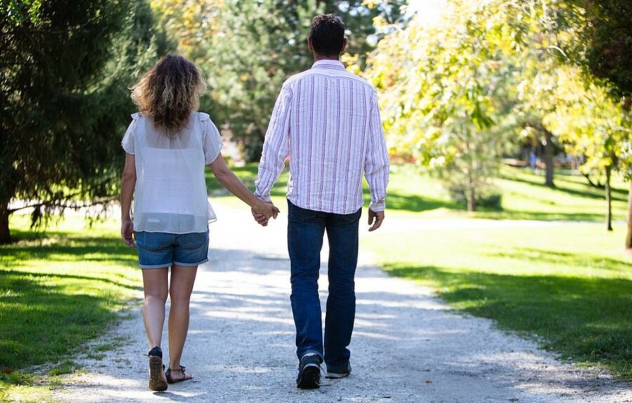 Couple holding hands walking through a green natural setting, perfect for a romantic camping weekend for two.