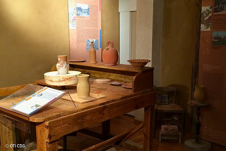 Exhibition space at the Angonia Museum in Martres-Tolosane, featuring an earthenware workshop with a potter’s wheel and handcrafted pieces.