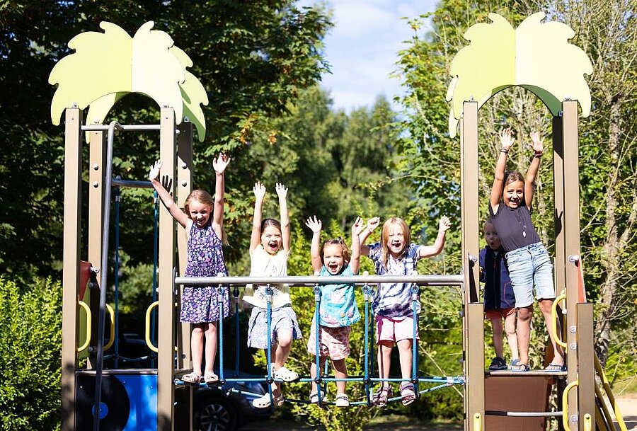 Children playing on a playground at a campsite, joyful family holidays in a safe natural setting.